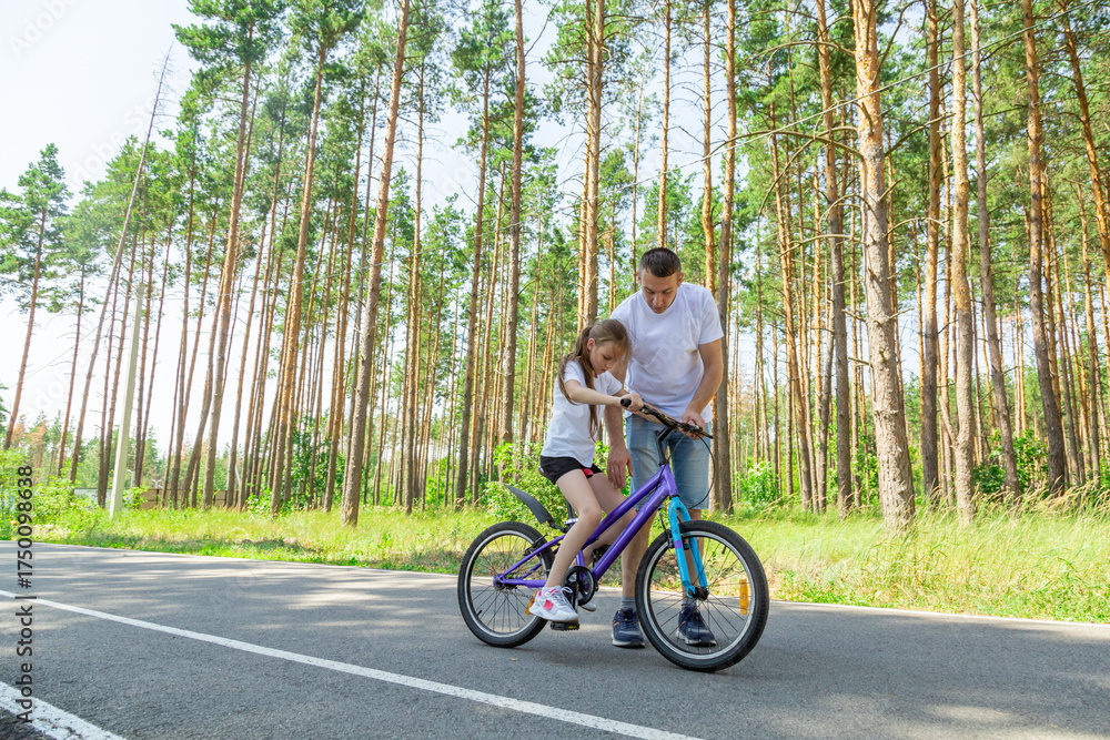 Fototapeta premium Father teaching his daughter how to ride a bicycle in forest