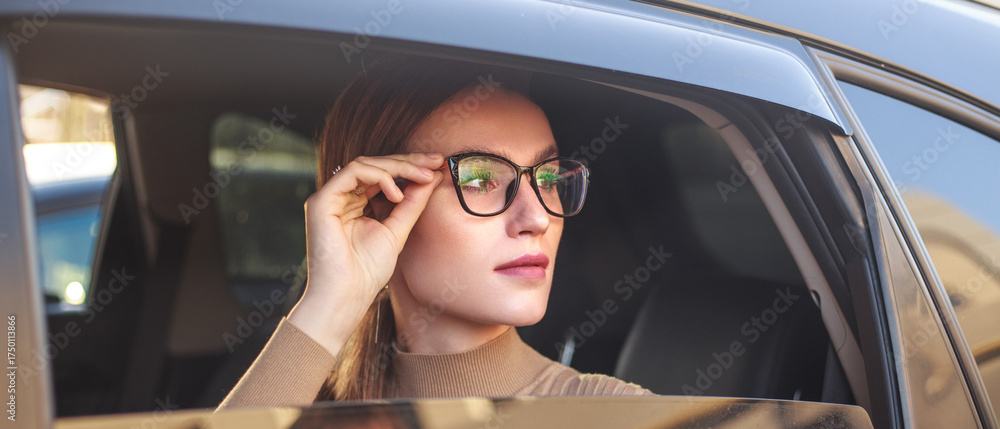 Naklejka premium Young, confident businesswoman wearing glasses looks out of car window with excitement