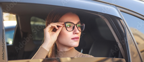 Young, confident businesswoman wearing glasses looks out of car window with excitement