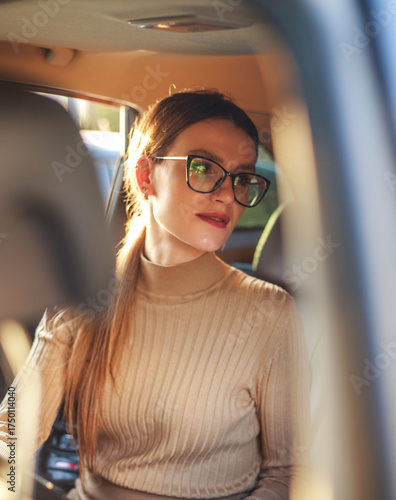 Young businesswoman sits inside car and looks at her partner, in warm sunlight