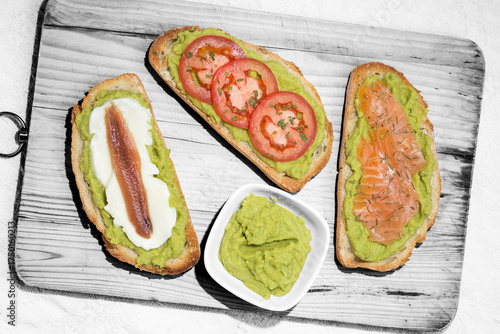 Different tapas: slices of bread with avocado, mozzarella cheese and anchovy, salmon and thyme, tomato and parsley,