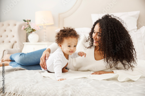 Happy mother and baby playing on bed in cozy bedroom. Bright morning light, love, tenderness, and family connection captured in natural home atmosphere.