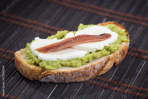 A slice of bread with avocado, lactose-free mozzarella cheese, and anchovy,