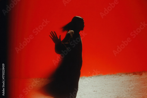 Silhouette of a person in motion against a vivid red background, creating a dramatic, mysterious scene with soft ground light and a sense of movement.