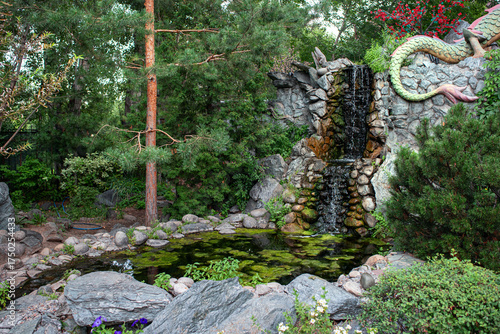 A small decorative waterfall, garden pond, trees, plants.