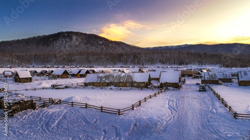 Winter Village Scenery in Hemu Xinjiang China at Sunset Snow Covered Landscape and Wooden Structures with Warm Evening Light Against Blue Sky