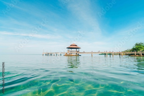 Fototapeta Naklejka Na Ścianę i Meble -  In the distance, against the backdrop of a clear blue sky, a cozy gazebo rises on the pier. It's the perfect spot for complete relaxation and a break from the hustle and bustle.