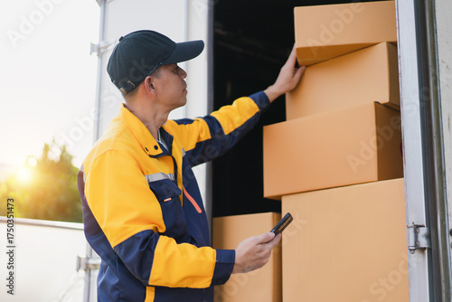 Delivery Worker Organizing Packages in Delivery Truck During Sunset with Smartphone in Hand for Inventory Management