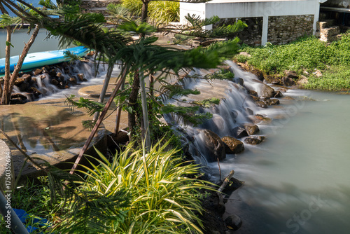 Scenic shot of a slow-shutter waterfall framed by soft-focus plants in the foreground. Taken at a serene resort in Nakhon Nayok, Thailand.