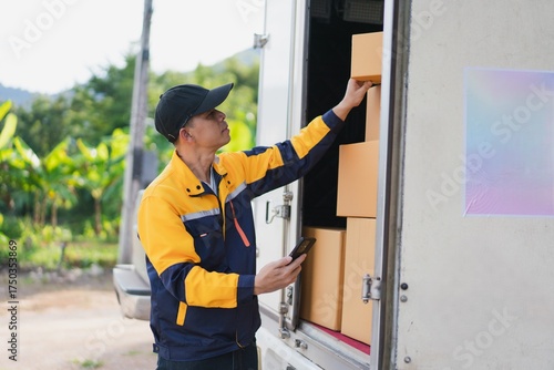 Delivery Person Organizing Packages in Truck with Smartphone in Green Landscape