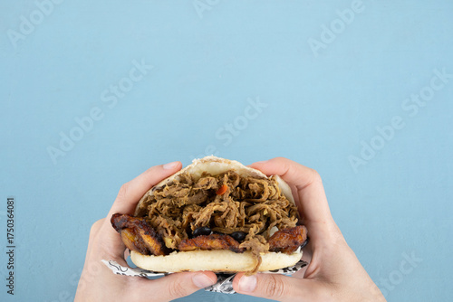 Hands holding an arepa made with beef, plantain, and beans with copy space.