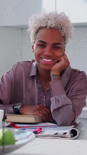 Confident female entrepreneur in a home office leans on her elbow among papers, planners and stationery, smiling directly at the viewer and conveying productivity, calm focus and a friendly