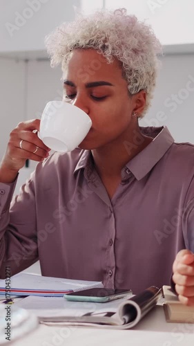 Solo African employee pauses to taste warm coffee during paperwork review, eyes closed in appreciation, surrounded by notebooks and printed reports on a tidy desk in a contemporary workplace setting.
