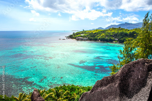 Turquoise Water in Seychelles, seen from a rocky Cliff surrounded by tropical Palmtrees