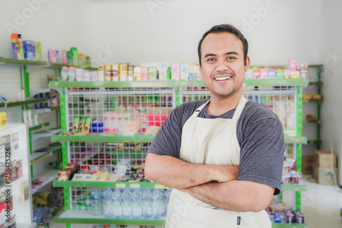 Smiling Asian young man as groceries or modern market staff standing with crossed arms and full of confidence in front of display rack