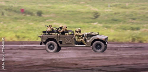 The specialized tactical vehicle transports soldiers with weapons mounted in the rear, moving swiftly over the unpaved ground during a training exercise with a blurred green landscape.