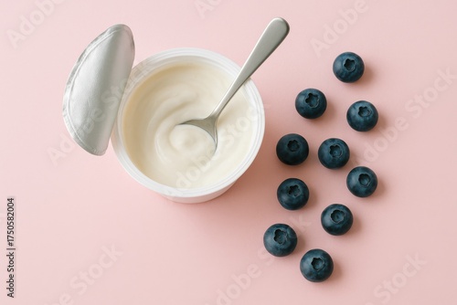 open greek yogurt cup with blueberries and spoon on pastel pink background in natural light, concept of healthy snack minimal composition and balanced nutrition aesthetic