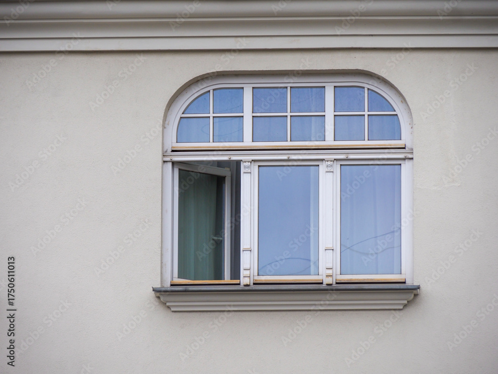 Fototapeta premium Close-up of a large arched window with white frames on a light-colored building facade