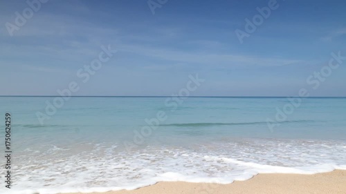A serene beach scene unfolds, with gentle waves caressing the shore under a clear, azure sky, capturing the essence of tranquility and the allure of a perfect coastal day.