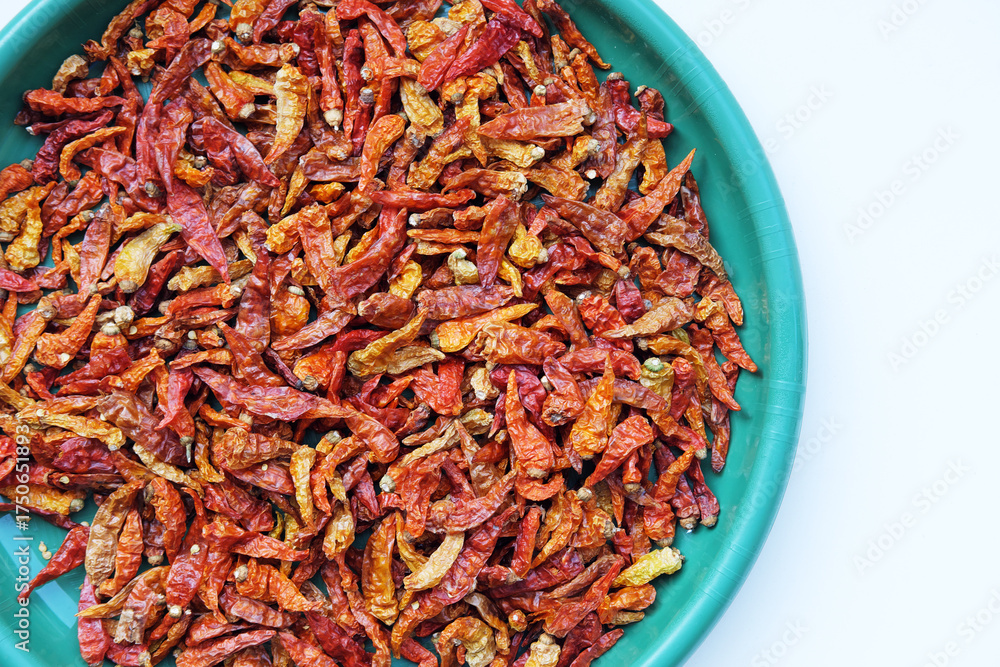 Fototapeta premium A top-down flat lay of dried red chili peppers in a turquoise plastic bowl, isolated on a clean white background with ample copy space.
