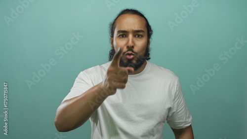 Man points finger directly toward camera in studio against teal backdrop, wearing a plain white t shirt; anger confrontation.