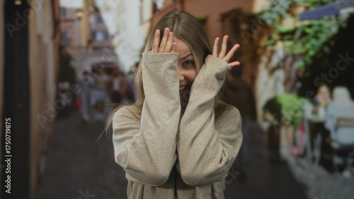 Woman covering face with hands in busy street while peeking through fingers; playfulness shyness curiosity innocence.