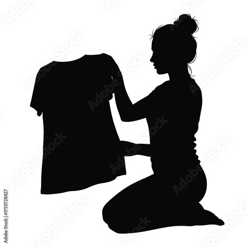A silhouette of a woman kneeling and holding a t shirt with a bun hairstyle in black and white