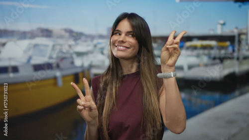Wallpaper Mural Young woman with long hair making peace signs at a marina with boats and a vibrant sea backdrop, showcasing a playful and relaxed outdoor summer scene. Torontodigital.ca