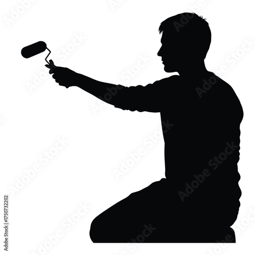 Silhouette of a man kneeling while holding a paint roller in his outstretched arm painting wall