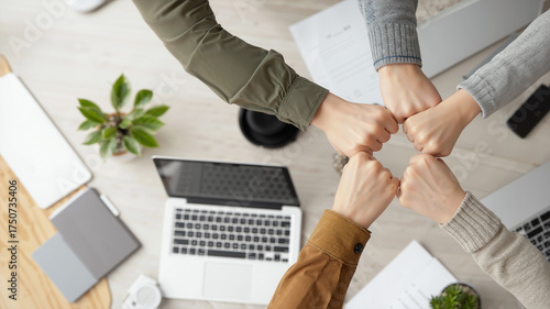 Wallpaper Mural A UGC-style, top-down photograph of a diverse team's four hands in a fist bump stack, symbolizing unity and collaboration over a modern office desk with laptops and equipment in the background. Torontodigital.ca