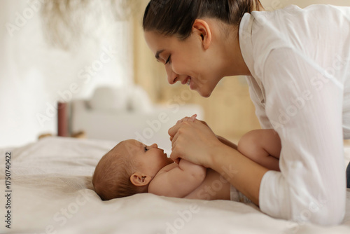 Young mother playing and chatting with her small child, holding kid's hands and looking at daughter. Happy motherhood with maternity leave