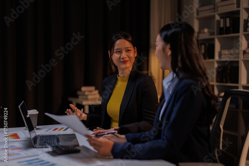 Billede på lærred In a dimly lit office, business asian women collaborate late into the night