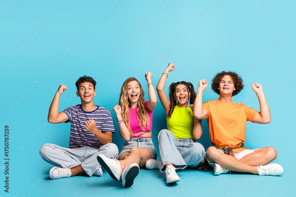 Obraz premium Group of four teens celebrate together on bright blue background full of energy and smiles