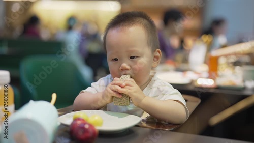 Asian baby eating cantaloupe in a restaurant, seated in a high chair, one-year-old boy