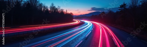 Winding road with colorful light trails at twilight. Trees line the road against a backdrop of mountains and a blue sky with clouds. The scene captures a serene moment of motion and transport.