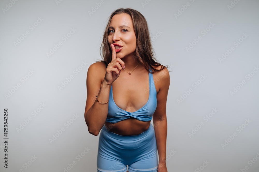 Obraz premium portrait of young woman in a blue outfit signals for silence with her finger on her lips on white background