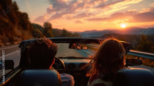 Two friends enjoy a scenic drive in a convertible during sunset. The road winds through mountains offering stunning views as the sun sets on the horizon.