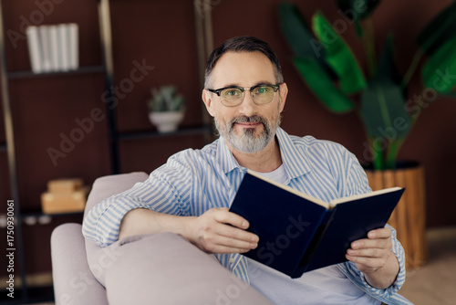 Mature man reading a book with confidence in a cozy living room setting showcasing indoor leisure and relaxation