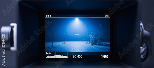 Professional videographer viewfinder displaying empty stage with drum set and microphones. Live event production and music concert record concept.