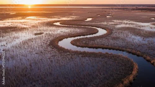 Serpentine River Winds Through Marshland During Golden Hour Sunset with Warm Orange Sky and Silhouetted Vegetation
