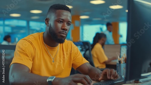 Focused Professional Working at a Computer in a Modern Office Environment, Engaged in Task as Colleagues Collaborate in the Background