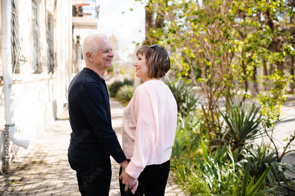 Naklejka premium Senior happy couple of stylish man and woman 60-65 year old walking together on streets holding hands at city outdoors. Wellness lifestyle. Happiness.