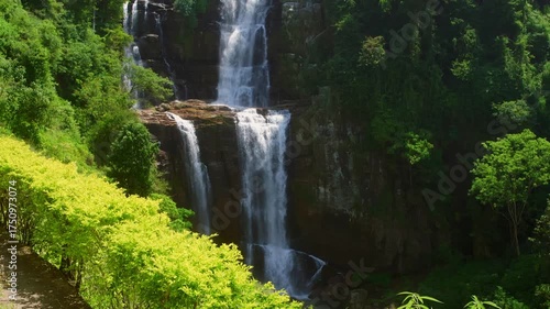 Cascading water plunging through rocky cliff face, surrounded by lush tropical vegetation and verdant greenery, revealing serene natural landscape in pristine wilderness setting