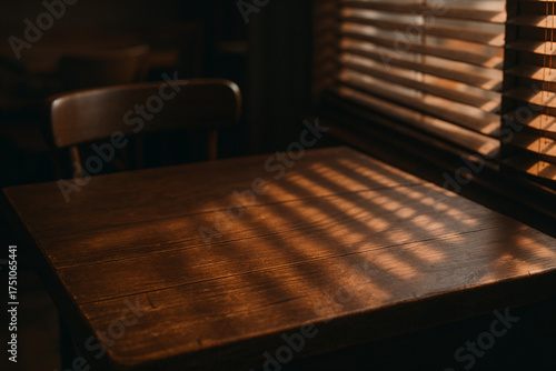 Warm light filters through window blinds onto a wooden table and chair, creating a cozy, nostalgic atmosphere in a quiet room.