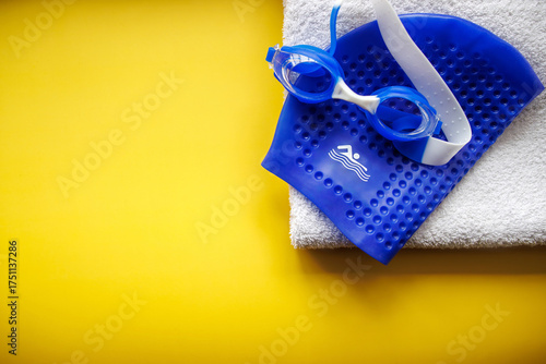 Swimming goggles and a blue cap with a towel on a yellow background, top view
