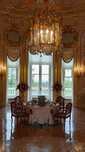 A vertical, medium-telephoto, indoor shot captures a lavish dining room or private chamber with a set table, illuminated by a glittering gold and crystal chandelier and bright natural light streaming