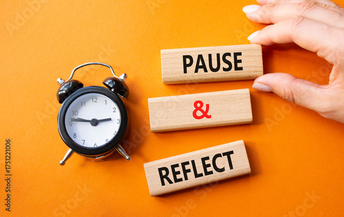 Pause and Reflect symbol. Concept words Pause and Reflect on wooden blocks. Businessman hand. Beautiful orange background with alarm clock. Business and Pause and Reflect concept. Copy space.