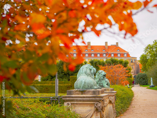 Autumn leaves frame the view of Rosenborg Castle in Copenhagen, Denmark. Historic lion statues guard the path to this iconic Scandinavian landmark.