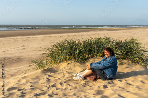 Quadro su tela lonely woman sitting behind reed grass in the slipstream on the sand dunes sways