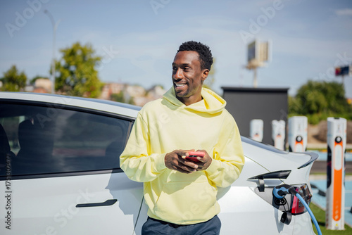 Young man smiling while charging electric vehicle